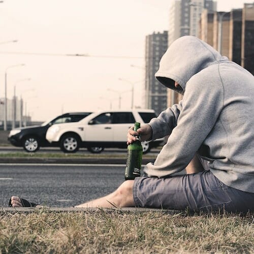 A sad man in a hoodie sitting on the side of the road.