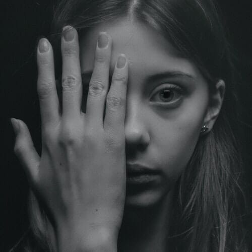A black and white photo of a girl covering her face with her hands.