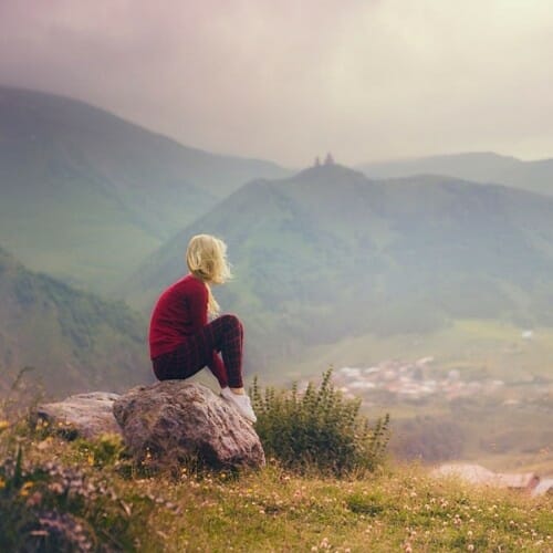 A woman sitting on a rock overlooking a valley with a sad expression, displaying her Whatsapp DP (display picture).
