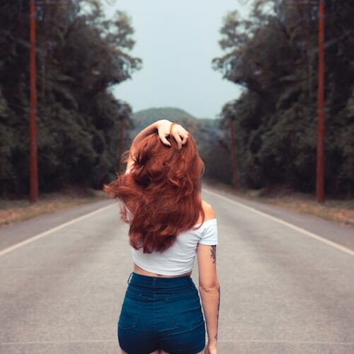 A woman with red hair standing on a road.