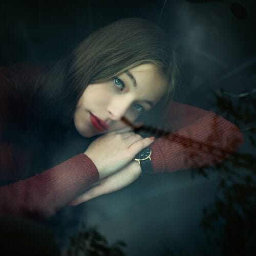 A girl in a red sweater leans against the window of a car.